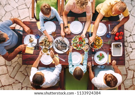 Big family have a dinner with fresh cooked meal on open garden terrace