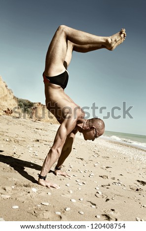 Yoga practice.  Man in scorpion yoga pose on the beach