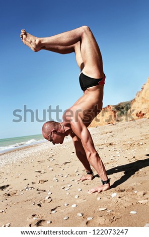 Yoga practice. Muscular man doing scorpion yoga pose at the deserted beach