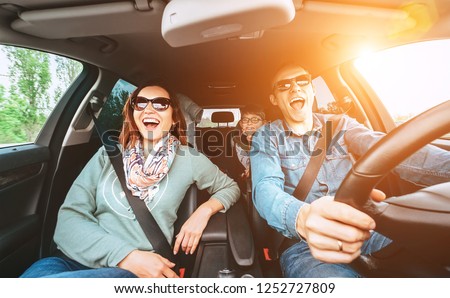 Cheerful young traditional family has a long auto journey and singing aloud the favorite song together.  Safety riding car concept wide angle view image.