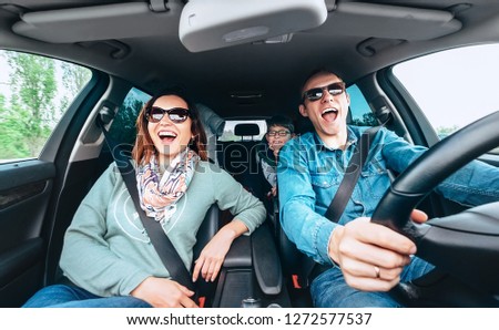Cheerful young traditional family has a long auto journey and singing aloud the favorite song together. Safety riding car concept wide angle inside car view image.
