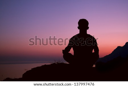 Sitting man silhouette on the top of hill in meditation pose