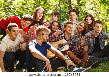 Group of young people singing by guitar in summer park