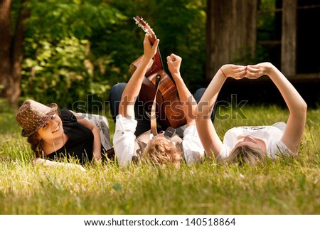 Happy teenage friends relax with guitar music on the green meadow