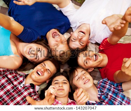 Circle of happy smiling teenage school friends lying on the grass