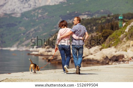 Love couple walking with beagle puppy on the sea coast
