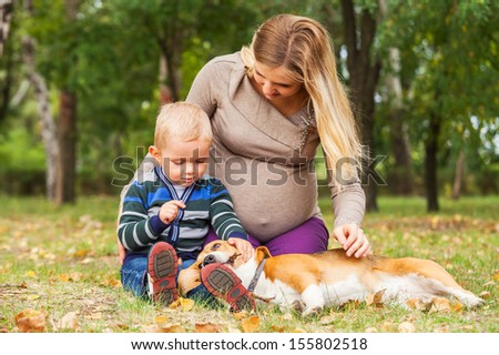 Pregnant mother with little son playing with pet in autumn park