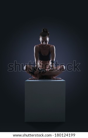 Slim woman sitting on white cube in cocke yoga pose