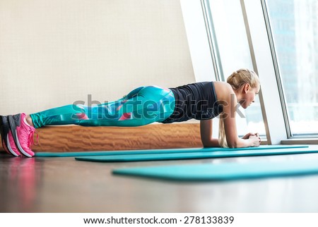 Blonde female doing plank static exercise in gym