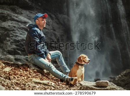 Man with dog sitting near waterfall