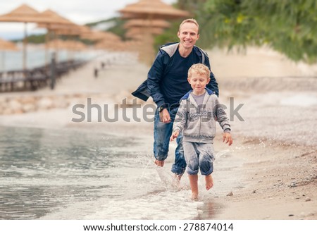 Little boy running with his father at the surf line