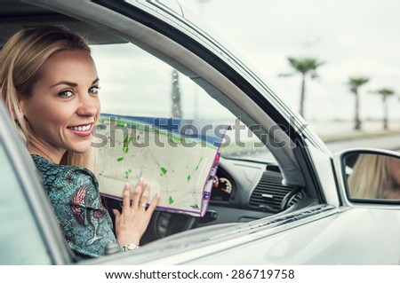 Pretty young woman sitting in car with a roads map