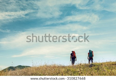 Two mountain travelers with backpacks under blue sky