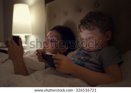 Mother with son lying in bed and look in their electronic device