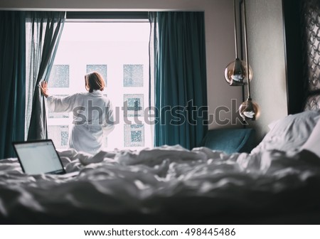 Woman in white robe stay hear the window in hotel room