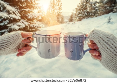 Couple hands in mittens take a mugs with hot tea in winter forest