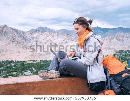 Backpacker female with laptop sits on the top view point under mountain settelment