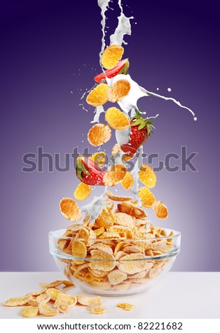 Gold corn flakes and the strawberry falls into the bowl with jets of milk on dark purple background