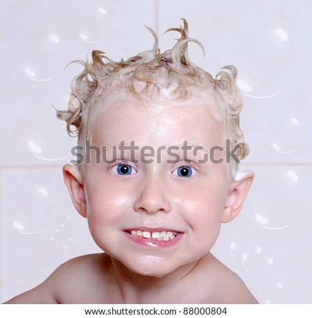 funny boy with soapy head and soap bubbles in the bathroom