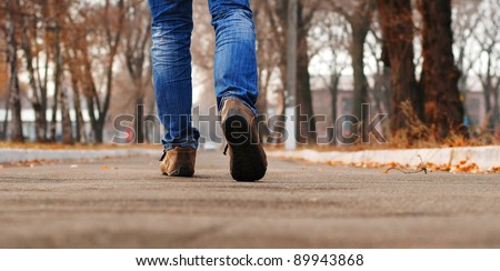Close up view on man\'s legs in blue jeans and boots walk through autumn park alley