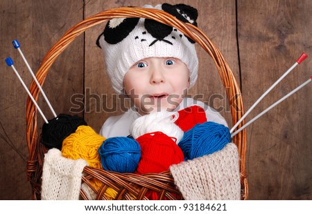 Surprised funny boy in knitting panda hat with wool yarn into basket