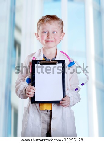 Cute little boy in doctor uniform with clip board in hands on light blue hospital background