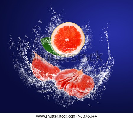 Red juice pieces of grapefruits with leaves in water splashes on the dark blue background