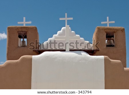 Four white crosses against a blue sky atop an adobe church in a pueblo in New Mexico.