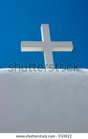 White cross atop a white adobe church against a blue sky in a pueblo in northern New Mexico.