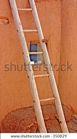 Old wooden ladder with a missing rung leaning against an adobe wall of a building in a pueblo in northern New Mexico.