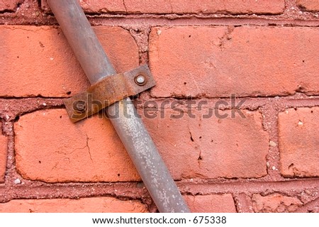 Metal strap holding a piece of electrical conduit to a red brick wall.