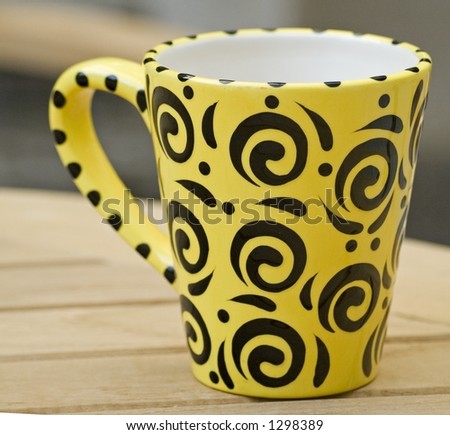 Yellow and black coffee mug on a wooden table in a garden.