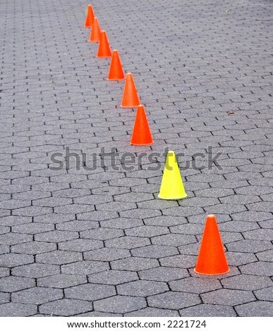 Six orange and one yellow caution cones on a path made of hexagonal blocks in Central Park in New York City.