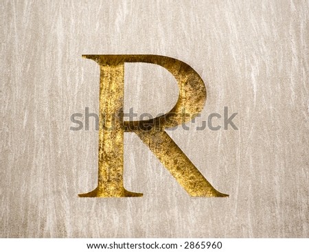 The letter R chiseled into a block of granite and embossed with gold paint.