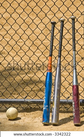 Softball and three bats leaning against a fence at a ball field in Central Park in New York City.