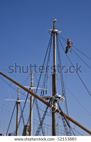 Man suspended in a bosun\'s chair repairing the rigging of an old square rigged wooden sailing ship.