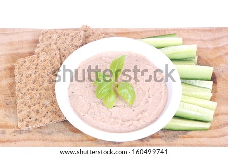 A tuna fish dip garnished with basil leaves in a bowl surrounded  by English cucumber sticks and crisp bread on a wooden board. Image isolated on white studio background.