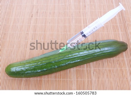 A whole green English cucumber injected with syringe on bamboo background.