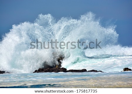 A splashing big wave crashing into the rocks in the rough wild water of the Indian Ocean on a stormy sunny day during springtime in South Africa.