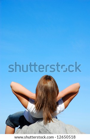 Rear view of a caucasian young woman relaxing by lying on the rocks watching the blue sky outdoors