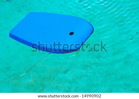 An abandoned blue surfboard floating in a dirty swimming pool outdoors after the end of the season