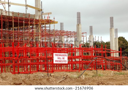 A building site with a big red and grey big scaffolding with yellow warning sign TRESPASSERS WILL BE PROSECUTED outdoors