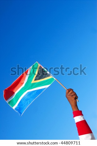 Black male hand of an African American soccer fan holding up the South African flag in front of blue sky background