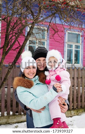 Beautiful family in warm clothes standing  of his house in winter