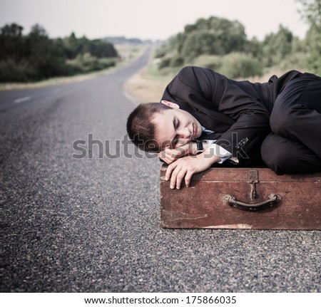 young man lies on the old suitcase on the road