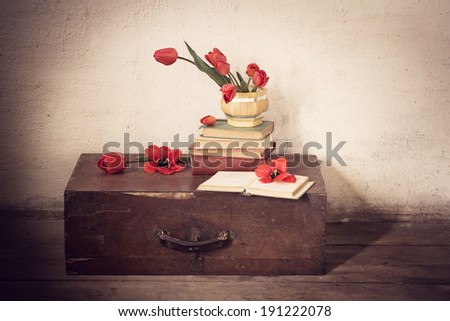 Vintage old suitcase with old books and red tulips  on floor
