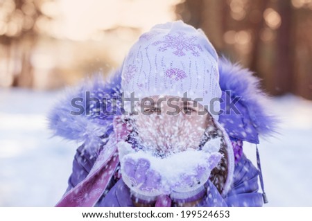 cute little girl in warm hat and gloves blowing snow