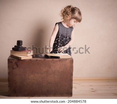 little girl reading a book on the old suitcase