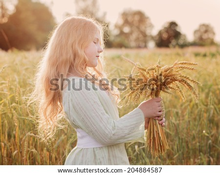 Happy child holding wheat ears at field