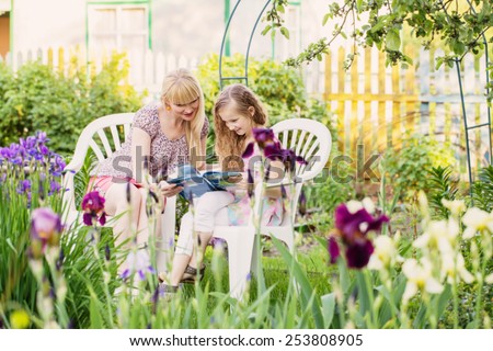 portrait of a beautiful young mother and her daughter reading book in garden